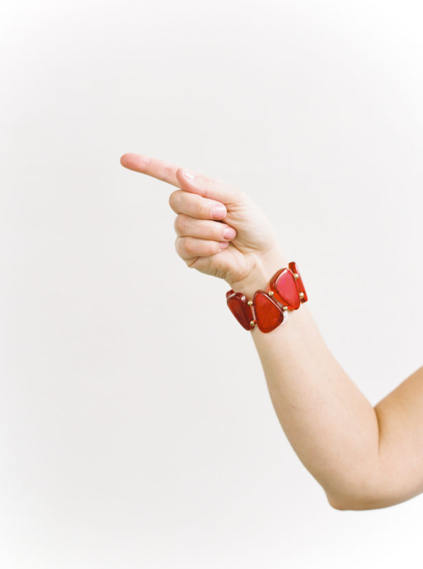 A woman's hand and arm, wearing a red jewel bracelet, pointing to the left.