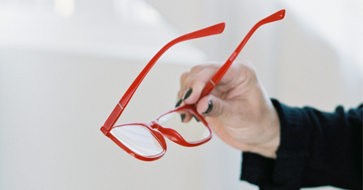 A woman's hand holding a pair of bright red glasses.