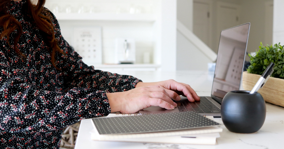 Woman's hands resting on laptop keyboard. She is sitting at a kitchen island.