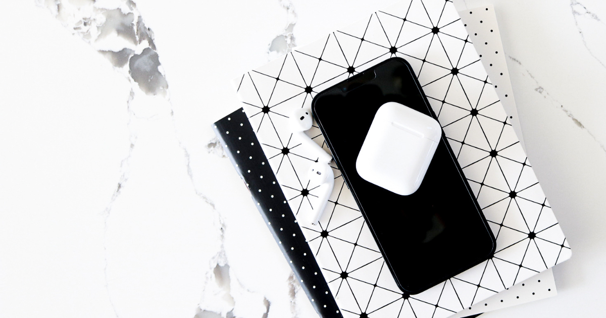 an airpod case sitting on top of an iPhone with notebooks underneath.