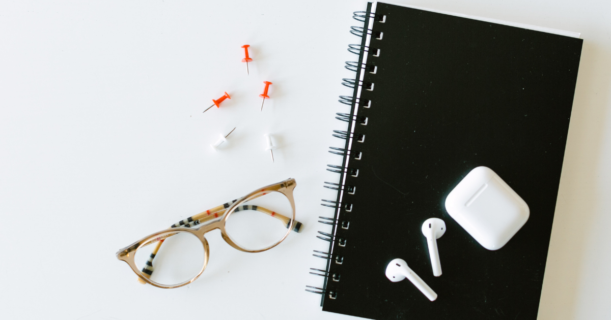 A pair of Apple Airpods sitting on top of a black notebook with a pair of glasses next to it.