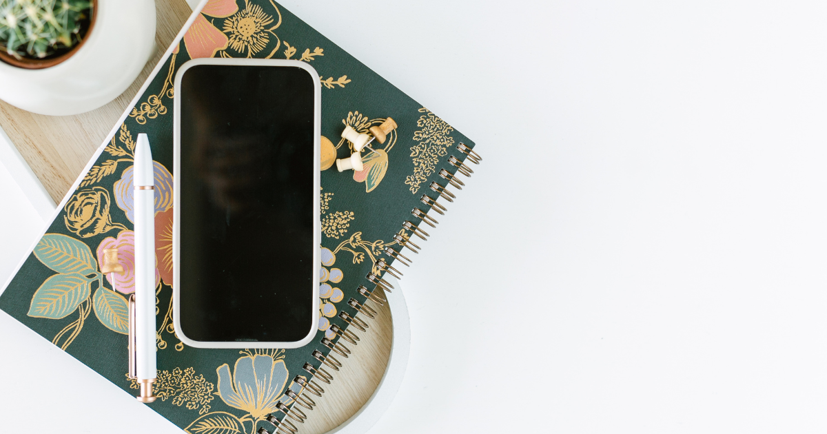 An iPhone sitting on top of a floral notebook.