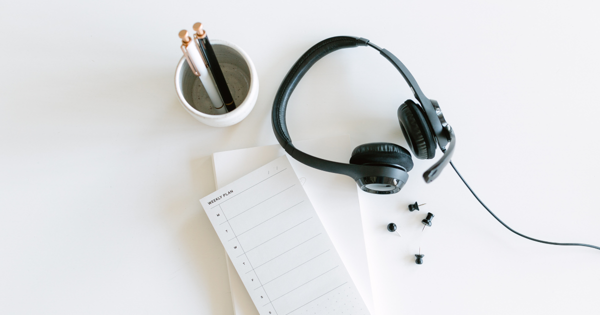 A pair of headphones sitting next to a notebook with some pens.